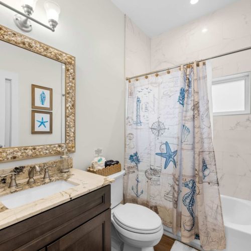 Guest bath: a shell-framed mirror and tub-shower combo with coastal charm.