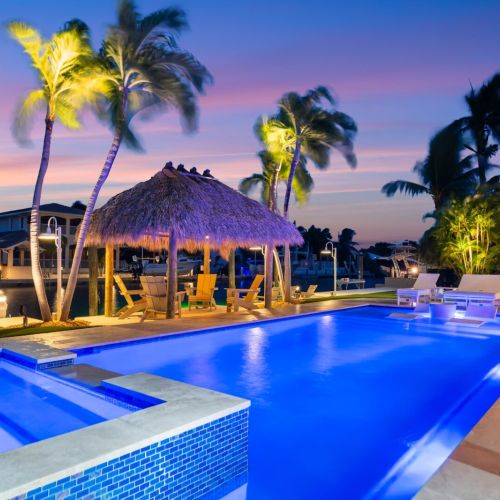 Blue hour perfection. Sip a drink under the tiki hut while the pool glows beside the water.