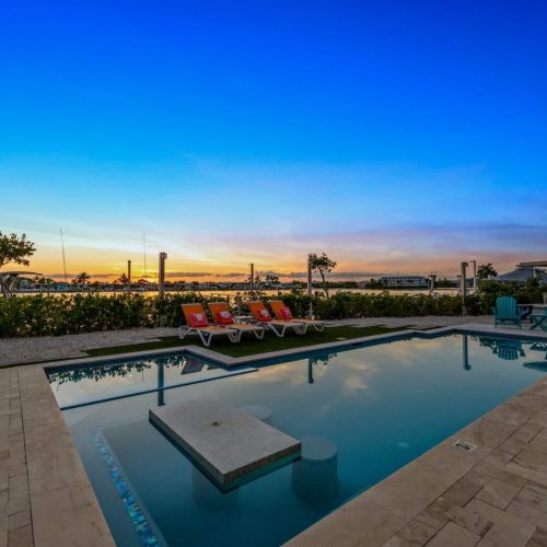 Travertine pavers frame the heated pool and sun shelf under a golden keys sky.