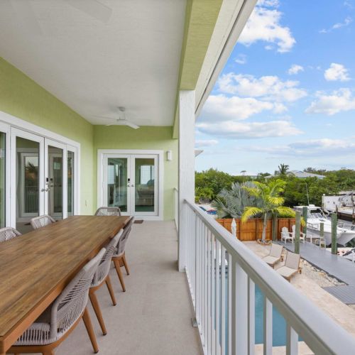 Covered balcony: a long alfresco table over the pool, dock, and canal beyond.