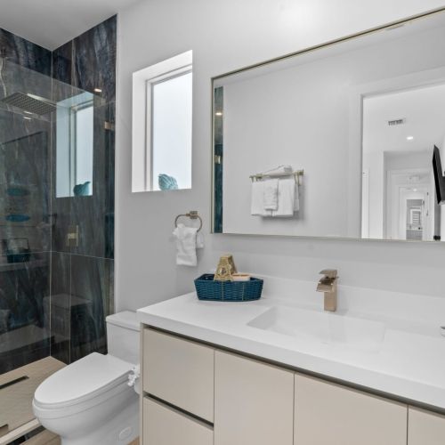 Step into luxury with this fully-equipped bathroom featuring a sleek shower, modern toilet, stylish sink, and a large mirror for all your grooming needs.