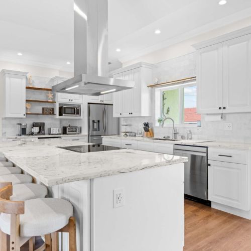 Chef's kitchen: bright white cabinetry, marble counters, and a statement range hood.