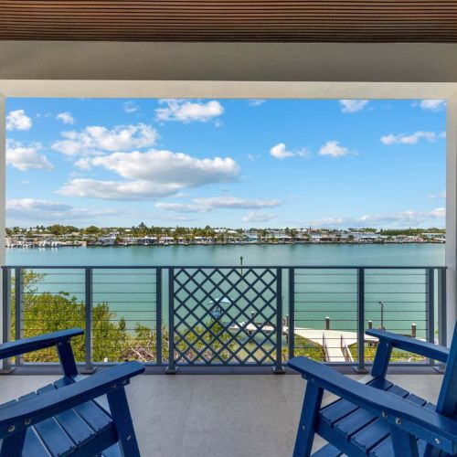 Navy adirondack chairs beneath a wood-slat ceiling frame a turquoise water panorama.