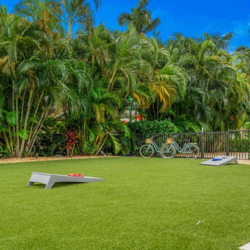 Private lawn with cornhole and bikes, surrounded by tropical palms for total backyard hangout vibes.