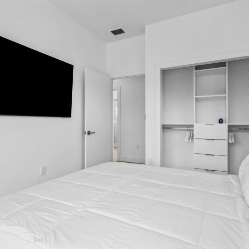 Bright minimalist bedroom with a large smart tv and built-in closet storage