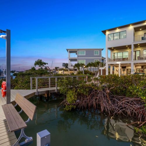 A lit composite dock with bench seating leads through mangroves to the water.