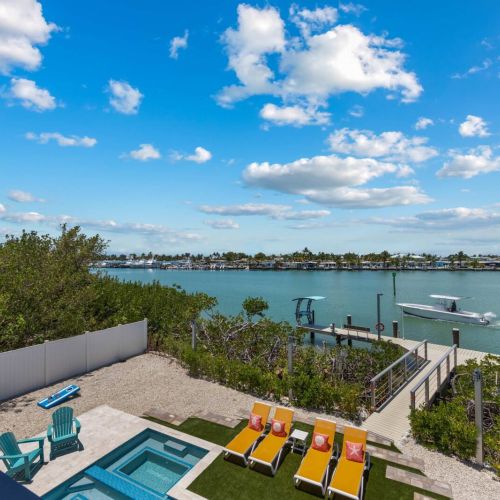 The upper level overlooks the glowing pool, sun loungers, and boats cruising past the dock.