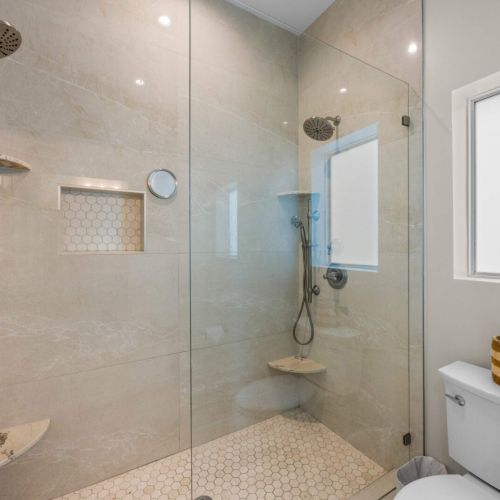 Walk-in shower: dual shower heads and a built-in bench in marble-look tile.