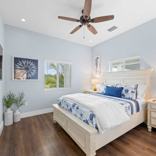 Bedroom 1: a coastal blue room with a queen bed, seahorse art, and garden views.