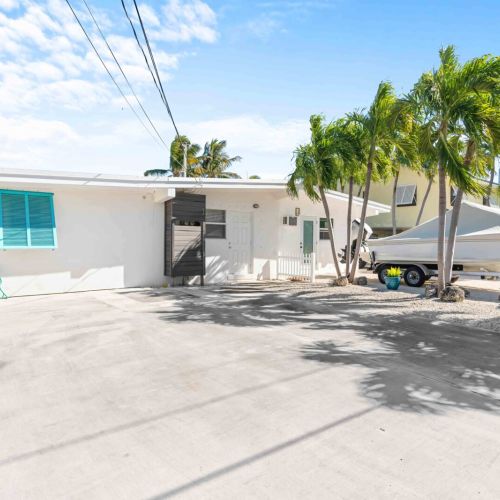 Escape to your perfect getaway! This charming white building stands under a beautiful blue sky, surrounded by refreshing palm trees. Enjoy a relaxing stay in this cozy retreat, where sunny days and breezy afternoons await you.