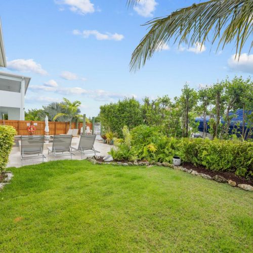 Backyard lawn: a green patch of yard bordered by tropical hedges beside the pool.