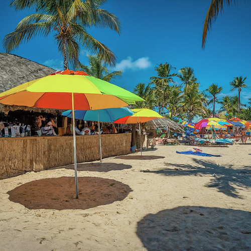 People relaxing on the beach at Sombrero Beach in Marathon, Florida, with colorful umbrellas providing shade.