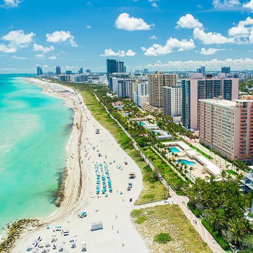 Scenic beach in Marathon, Florida, with colorful buildings lining the shore and palm trees in the foreground.