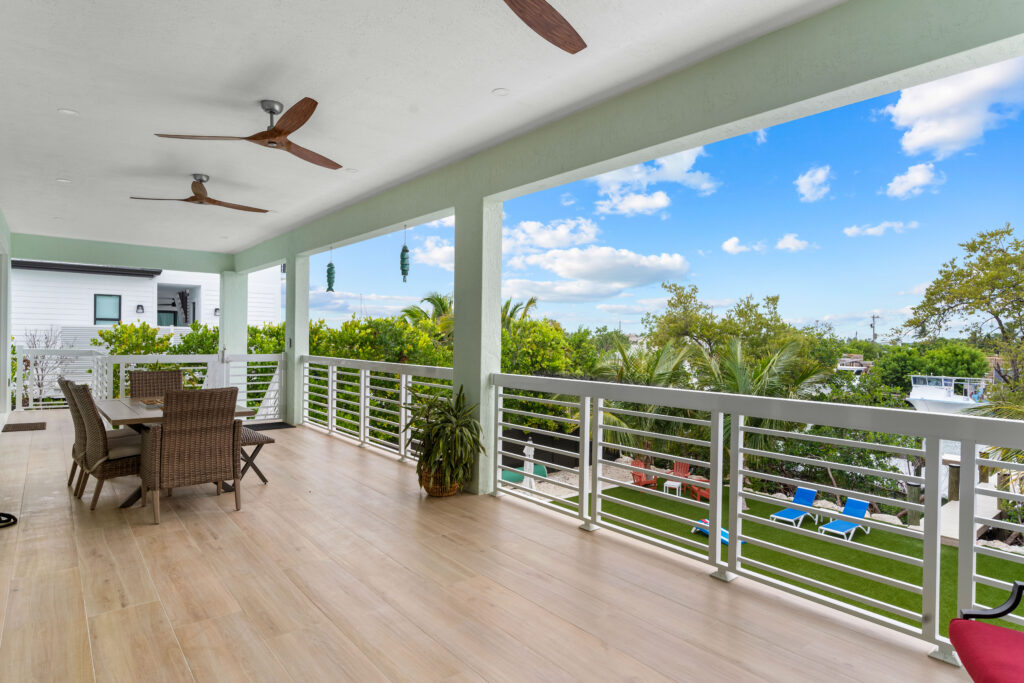 Spacious outdoor balcony at Emerald Oasis in Marathon, Florida, featuring a dining area with a scenic view of lush greenery and clear blue skies, perfect for vacation rentals.