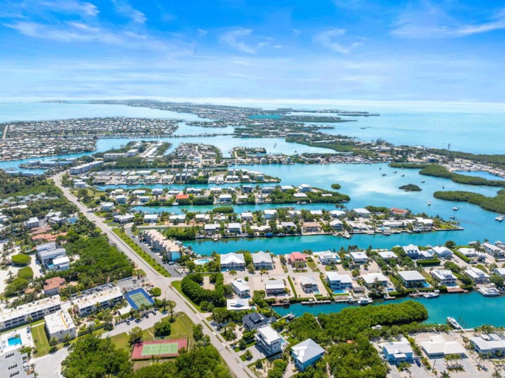 10 nature trails & parks in marathon fl | wild side guide 13 Aerial view of a coastal town with houses surrounded by water canals, lush green trees, and clear blue skies, overlooking the ocean and distant islands.