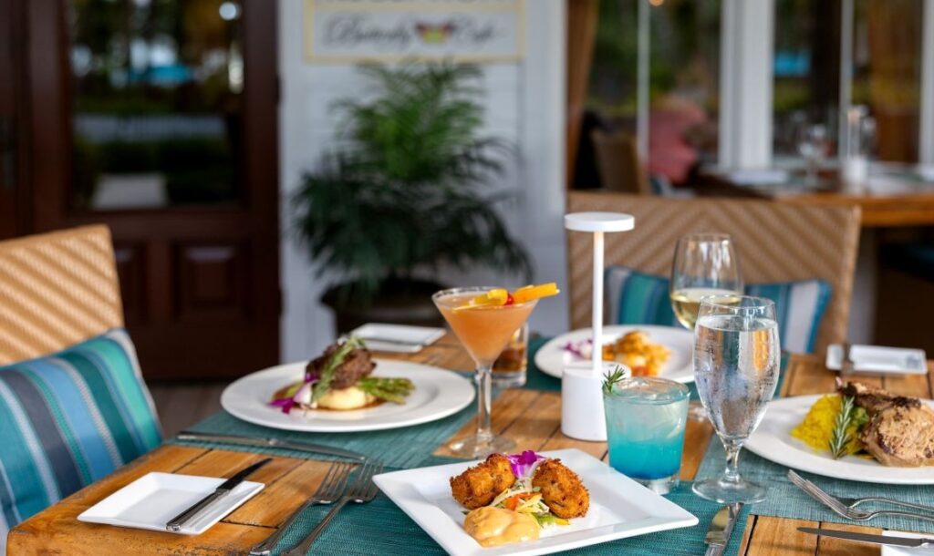 9 romantic anniversary ideas in marathon, fl | couples getaway guide 4 A restaurant table set for a meal with plates of gourmet food, cocktails, and water. The table has woven chairs with teal cushions, and the background shows a plant and part of an inviting dining area.