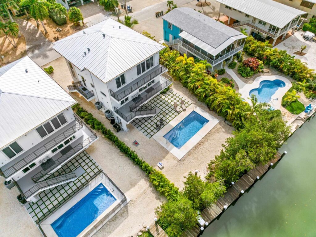 Aerial view of modern waterfront homes with private pools and docks along a canal. The white exteriors, metal roofs, and lush gardens highlight why marathon florida is perfect for snowbirds seeking sun-soaked luxury.