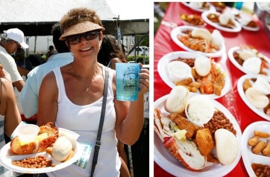 A smiling woman in sunglasses and a visor holds a tray with seafood, bread, and beans, along with a drink. Next to her are several plates of similar food on a red tablecloth at an outdoor event.