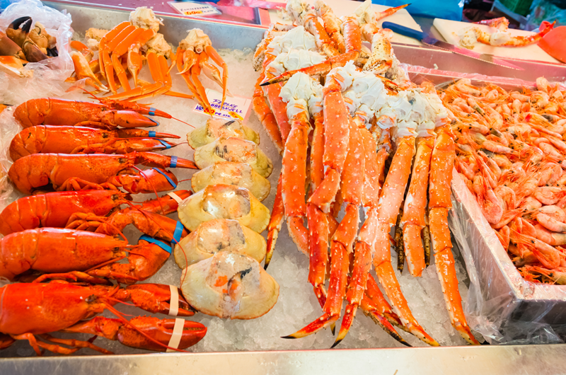 Fresh seafood on ice at a market, including whole lobsters, crab legs, split crabs, and a large pile of shrimp, displayed in rows for sale. (marathon fl seafood festival guide)