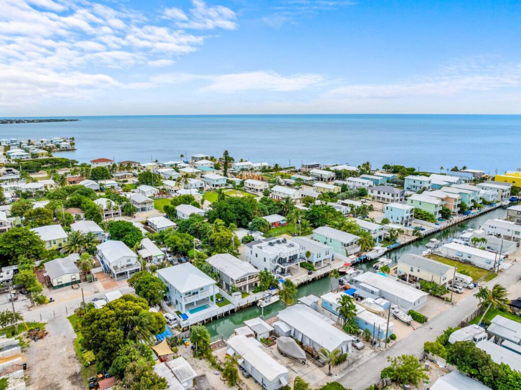 Vacation rental insurance 101 for marathon, fl owners (2026 guide) 6 Aerial view of a coastal town with white and pastel houses, lush green trees, and a canal running through the neighborhood, with the ocean and blue sky in the background.