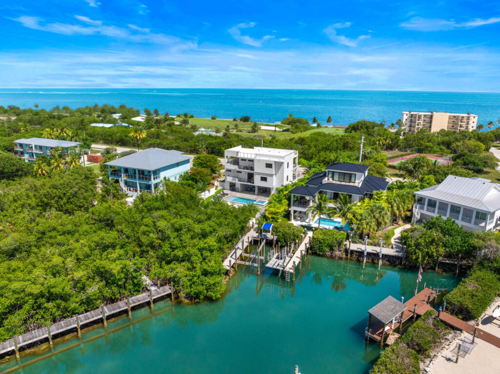 Marathon vs key west: which florida keys destination is right for you? 7 Aerial view of waterfront homes with docks along a calm canal, surrounded by greenery, with the ocean and blue sky in the background.
