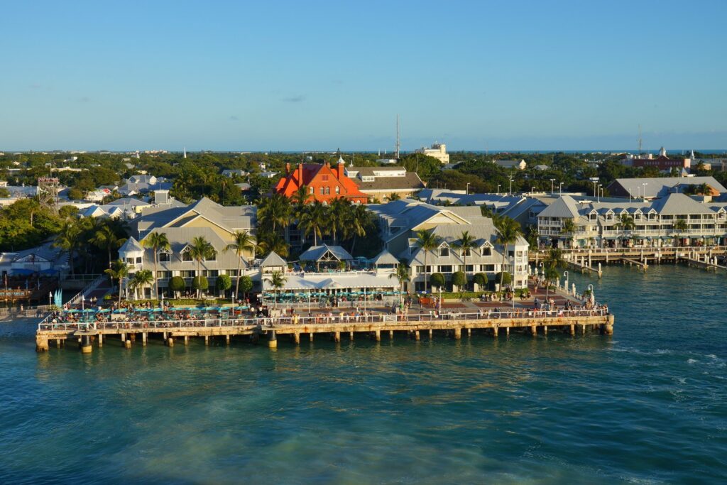 Marathon vs key west: which florida keys destination is right for you? 2 A waterfront resort with white buildings and palm trees sits along a pier in key west, florida. People are gathered on the pier, and the blue ocean water is in the foreground under a clear sky. Marathon vs key west