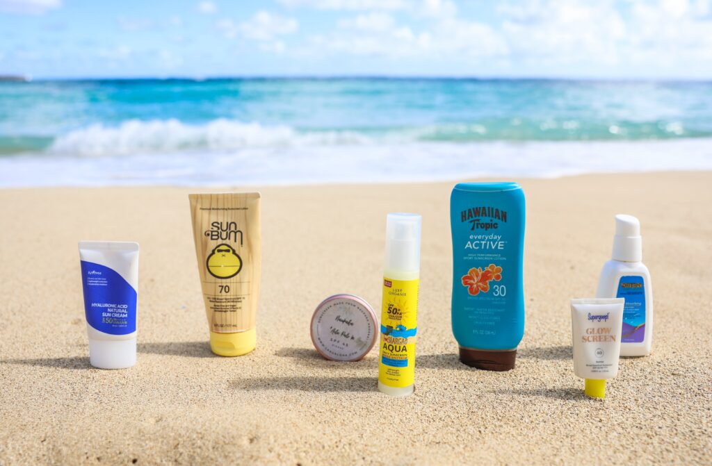 What to pack for florida keys: the only checklist (2026) 4 Various sunscreen bottles and containers are arranged in a row on sandy beach with ocean waves and blue sky in the background.