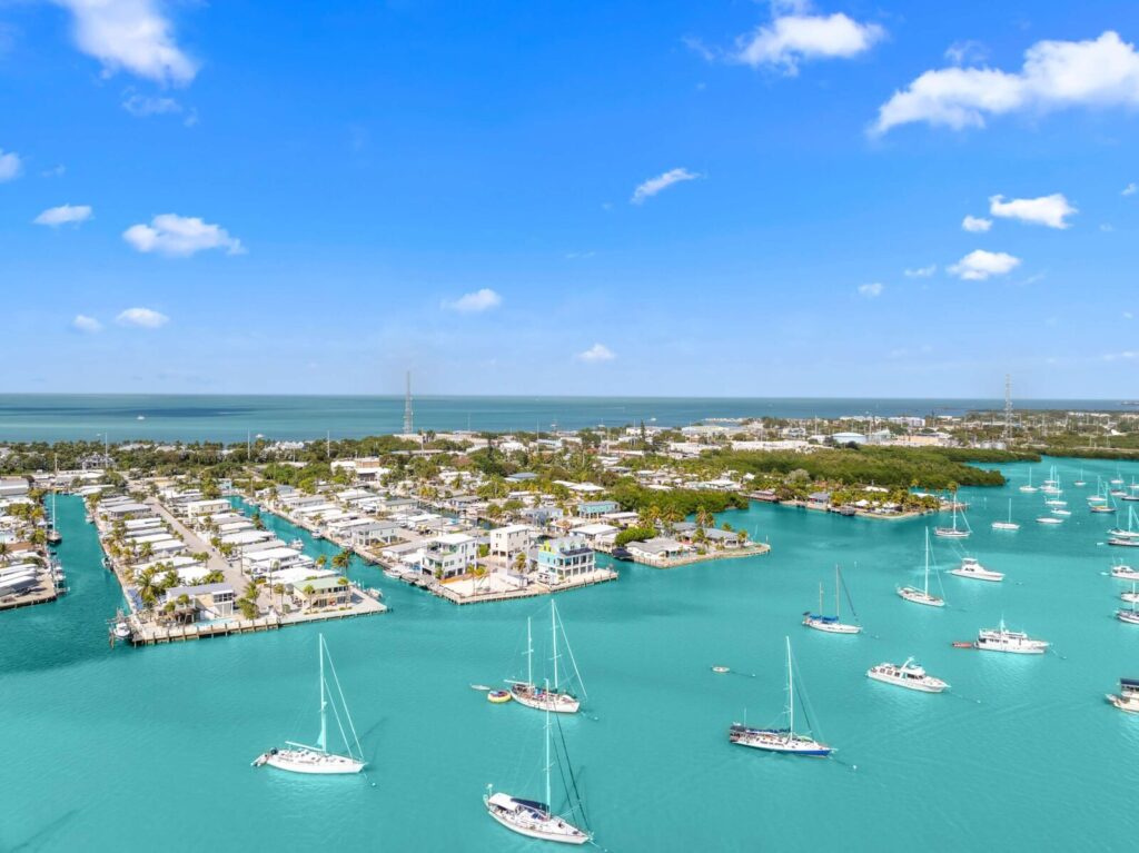 What to pack for florida keys: the only checklist (2026) 3 Aerial view of a marina with turquoise water, numerous sailboats and yachts anchored, and a coastal town with palm trees and buildings under a bright blue sky with scattered clouds.
