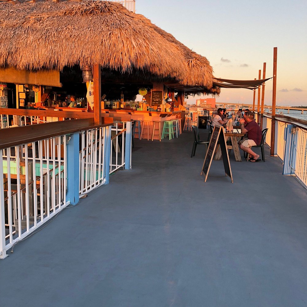 The ultimate marathon fl restaurants scene: from casual to fine dining 4 Outdoor beach bar with a thatched roof at sunset, tables and chairs with people dining, chalkboard menus, and a view of the ocean along a fenced walkway. Warm lighting creates a relaxed, inviting atmosphere.