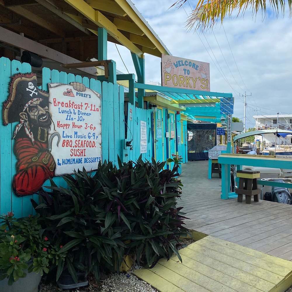 The ultimate marathon fl restaurants scene: from casual to fine dining 16 A colorful, beachside restaurant called porky’s with turquoise fences, a pirate mural, and a sign listing breakfast, lunch, dinner, and live music. Outdoor seating is visible, along with boats in the background.