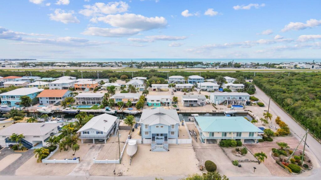Aerial view of a coastal residential neighborhood with pastel-colored houses, palm trees, and a canal running through the center under a blue sky with scattered clouds—an ideal setting for developing an effective vacation rental pricing strategy.