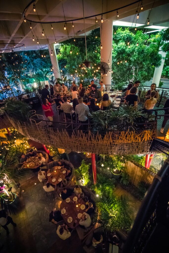 5 best restaurants in miami worth the trip | local picks 2026 5 A lively, two-level restaurant filled with people dining and socializing under hanging string lights, surrounded by lush greenery and warm, ambient lighting.