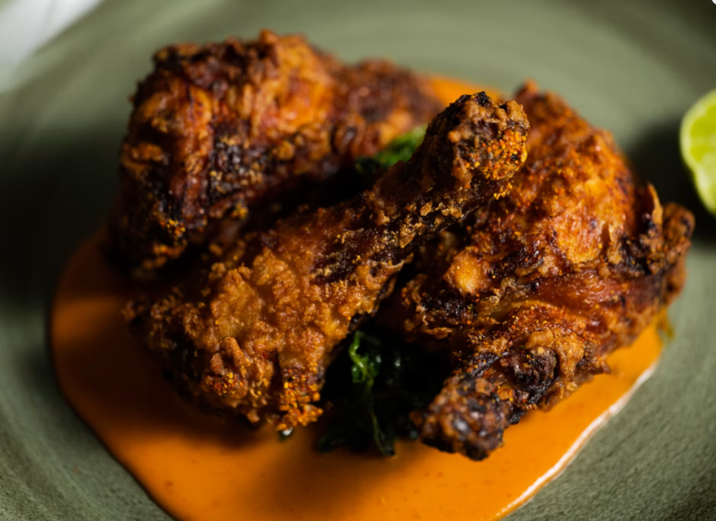 5 best restaurants in miami worth the trip | local picks 2026 6 Two pieces of crispy fried chicken rest on a plate, partially covered by a creamy orange sauce, with a slice of lime visible at the edge of the dish.