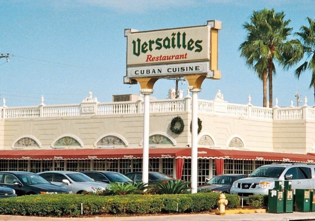 5 best restaurants in miami worth the trip | local picks 2026 3 A large sign reading versailles restaurant cuban cuisine stands in front of a cream-colored building with ornate trim, red awnings, and parked cars, likely the restaurant’s parking lot. Palm trees are visible nearby.