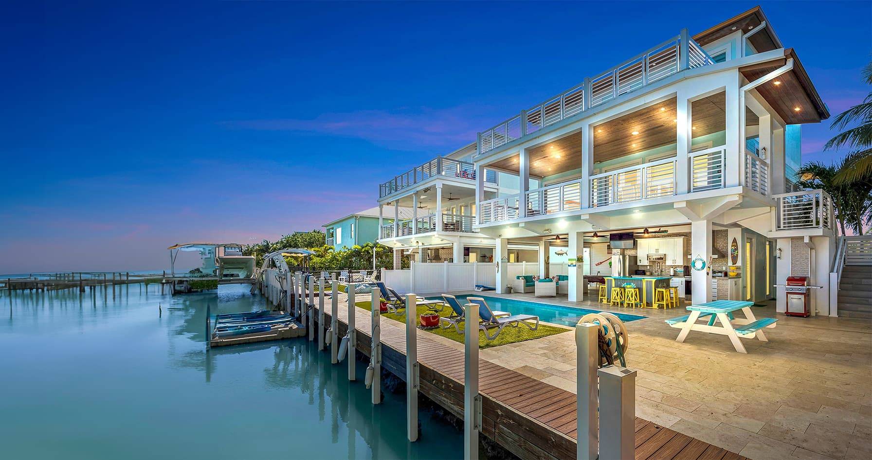 Luxurious waterfront vacation rental with a pool, balconies, and docked boats at dusk, creating a serene atmosphere