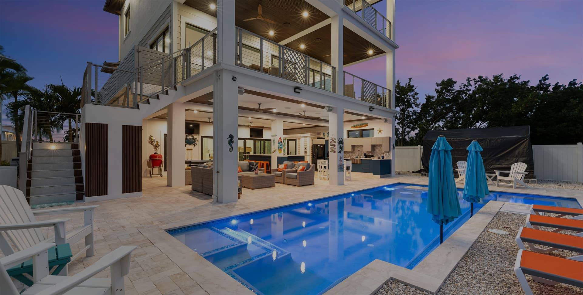 Luxurious waterfront property at dusk with a lit pool, outdoor seating area, and spacious balconies